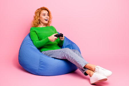 Young woman sitting on a blue bean bag while joyfully playing video games, dressed casually in a...