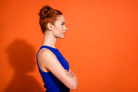 Profile of a Stylish Young Red-haired Woman in a Blue Top Against a Vibrant Orange Backgroundの写真素材