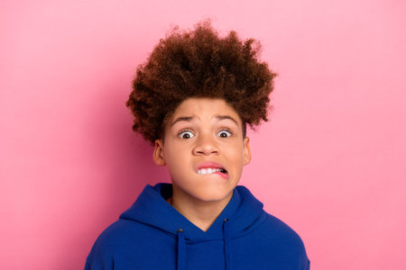 Portrait of a charming boy in a blue hoodie with a funny expression on a pink background, showcasing trendy casual styleの写真素材