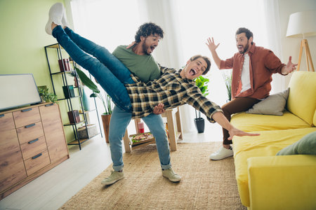 Full size photo of company three friends hang out play hands hold throw weekend modern interior apartment indoorsの写真素材