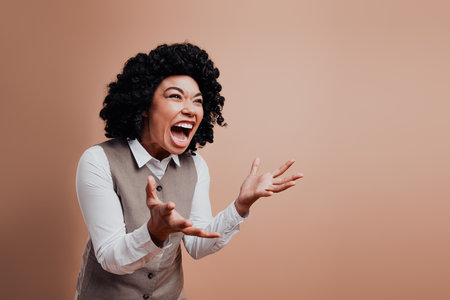 Confident businesswoman expressing strong emotions through gestures, wearing formal attire with a beige background.の写真素材