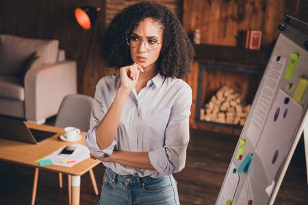 Confident businesswoman in modern office, pondering strategy with chart during daylight, embracing challenges of successful career.の写真素材