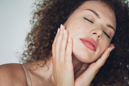 Beautiful young woman with curly hair embracing natural beauty and skin care with confidence and charmの写真素材