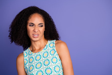 Young woman expressing distaste against purple background, wearing stylish summer top in vibrant floral design, showing candid emotionの写真素材