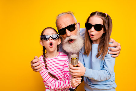 Grandfather enjoying time singing karaoke with his charming granddaughters on a vibrant yellow...