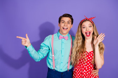 Retro couple in vibrant pin-up fashion smiling and gesturing enthusiastically against a violet backgroundの写真素材