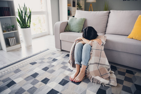 Young woman relaxing on a cozy sofa in the living room during a sunny day, wrapped in a blanket and enjoying a peaceful moment at homeの写真素材