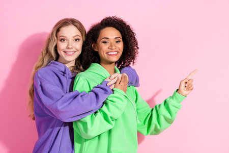 Two cheerful young women in colorful hoodies posing against a vibrant pink background, showcasing joyの写真素材