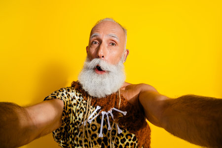Photo of aged savage caveman take selfie good mood wear leopard skin outfit isolated on yellow color backgroundの写真素材