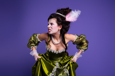 Elegant young woman in a historical green costume posing against purple background