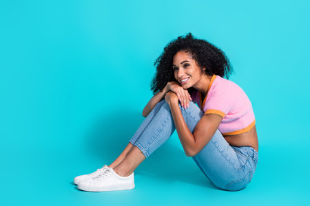 Attractive young woman in casual fashion sitting on turquoise background with a charming smileの写真素材