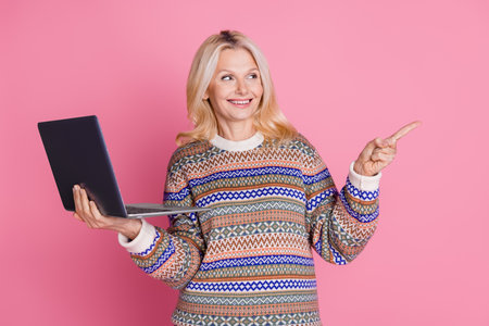Portrait of nice aged woman laptop indicate finger empty space wear sweater isolated on pink color backgroundの写真素材
