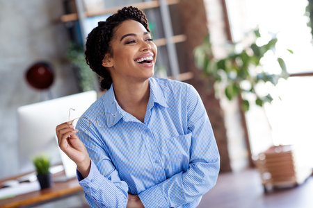 Smiling african american businesswoman holding glasses in modern office settingの写真素材