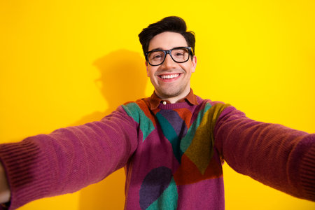 Smiling Young Man Taking a Colorful Self-Portrait Against a Bright Yellow Background Wearing Trendy Glassesの写真素材
