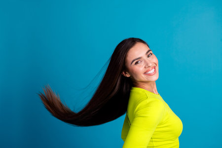 Smiling Woman Tossing Long Hair in Yellow Top Against a Blue Background, Radiating Happiness and Confidenceの写真素材