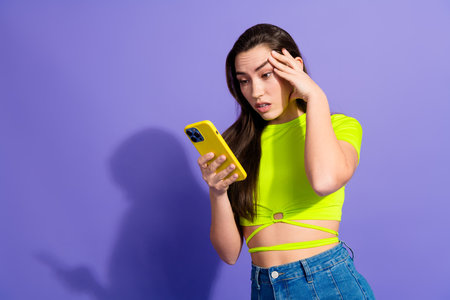 Young woman in vibrant neon attire checking her smartphone with a surprised expression against a...
