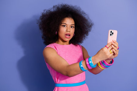 Stylish young woman with elaborate hairstyle expressing surprise while taking a selfie in pink...