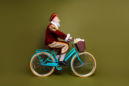 Elderly man in vintage costume on bicycle against green background showcasing a blend of medieval style and modern lifestyle.の写真素材