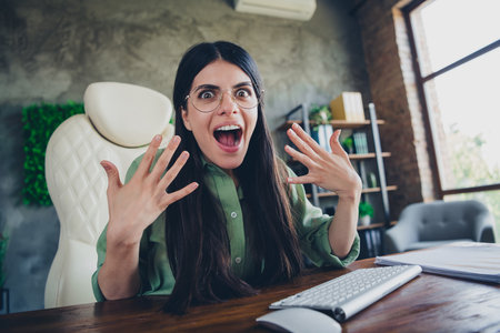 Excited young woman with brunette hair expressing joy while working in a modern office interior during daylight at her professional job.の写真素材
