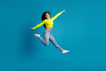 Smiling young woman in trendy casual clothes jumping joyfully against a vibrant blue background, radiating happiness and positivity.の写真素材