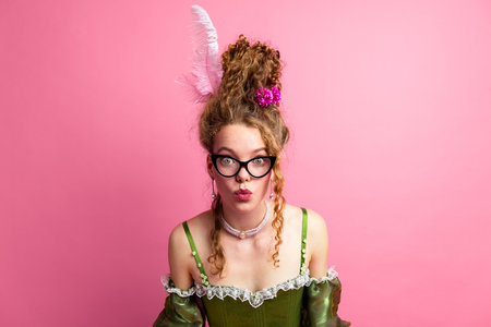 Elegant young woman in a green historic dress with a pink background showcasing a comparison between past and modern fashion stylesの写真素材