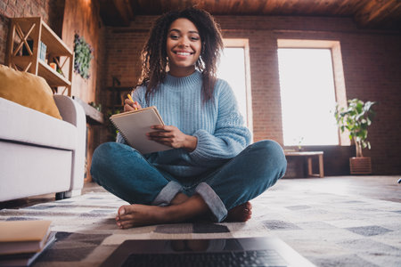 Young woman enjoying a cozy weekend at home, jotting notes in a sunny living roomの写真素材