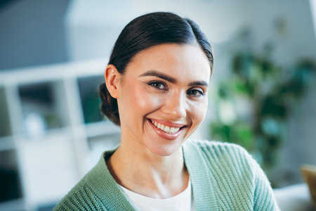 Portrait of a smiling young brunette woman indoors wearing a casual sweater in a cozy homey setting during daytime.の写真素材