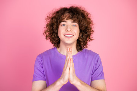 Young curly-haired man in a purple t-shirt smiling with a welcoming gesture against a vibrant pink backgroundの写真素材