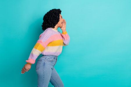 Young cheerful woman with curly hair in colorful pullover posing against a vibrant teal backgroundの写真素材