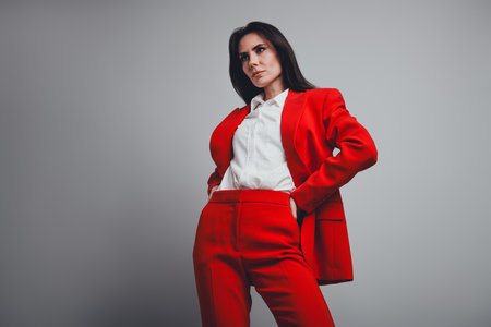 Confident businesswoman wearing a stylish red suit poses gracefully in a contemporary setting, exuding professionalism and eleganceの写真素材