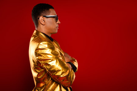 A charismatic young man in a glossy golden jacket confidently poses against a vibrant red background