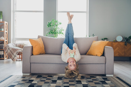 Young woman enjoying casual leisure time indoors on a cozy sofa in a stylish living room with natural daylightの写真素材
