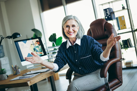 Confident mature businesswoman presenting in a modern office workspace with professional attire and charming demeanorの写真素材