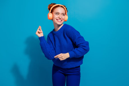 Charming young woman dancing joyfully in a blue sweater against a vibrant blue backgroundの写真素材