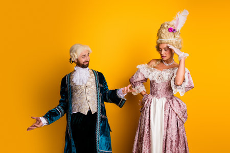 Elegant couple in vintage royal attire posing on vibrant yellow background illustrating historical nostalgia and modern comparisonの写真素材