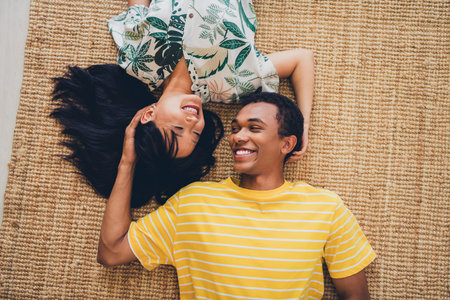 High angle view photo of lovely cute sweet multinational married couple wear t-shirts lying floor indoors flatの写真素材