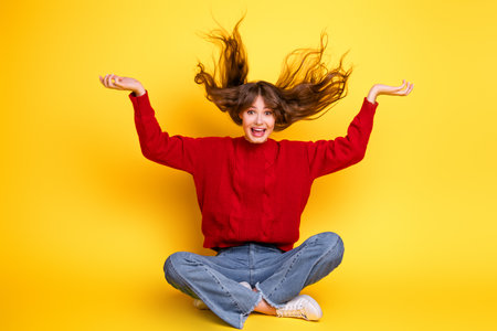 Playful Woman in Red Sweater Sitting on Yellow Backgroundの写真素材