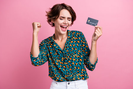 Portrait of ecstatic satisfied woman wear print blouse hold debit card win gambling scream yeah fist up isolated on pink color backgroundの写真素材