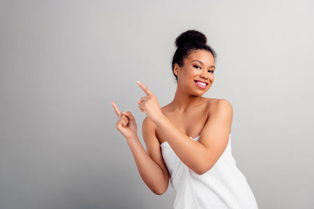 Smiling young woman wrapped in a towel pointing with excitement in a beauty studio settingの写真素材