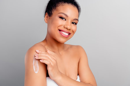 Smiling young woman applying skincare lotion to arm in a wellness and beauty sessionの写真素材