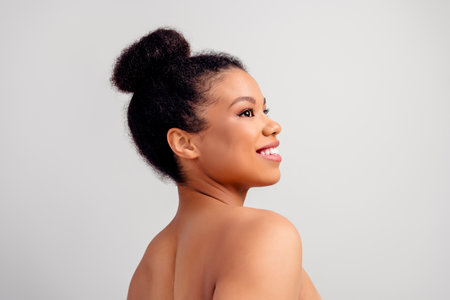Side profile of a young woman smiling with radiant skin and natural hairstyle against a grey backgroundの写真素材