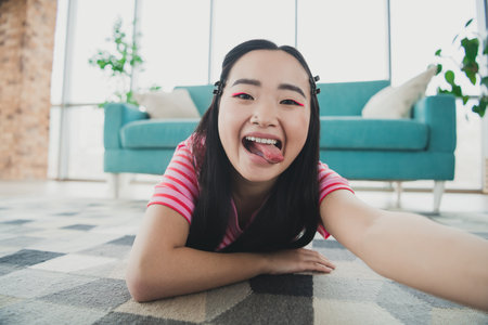 Young smiling woman lying on floor of bright living room, expressing playfulness and fun in a relaxed environmentの写真素材