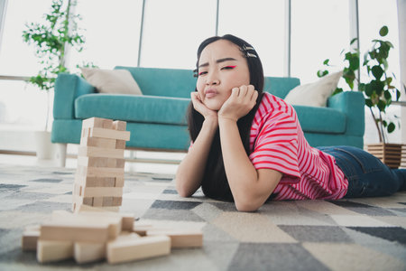 Young woman in a pink striped shirt relaxing on the floor in her cozy living room on a sunny day...