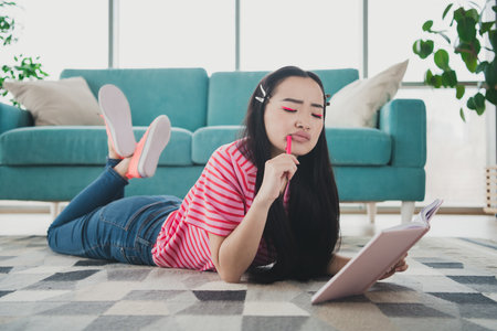 Young woman in casual clothing writing in a notebook at her living room, featuring a homey and relaxed atmosphereの写真素材