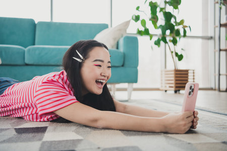 Joyful young woman enjoying leisure time on a weekend afternoon in a cozy modern living room while using her smartphone.の写真素材