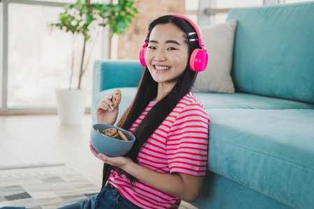 Young woman enjoying cookies while listening to music at home, showcasing a relaxed lifestyle indoors with bright colorsの写真素材