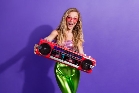 Young woman with blonde hair enjoying a retro dance party holding a vintage boombox against a...