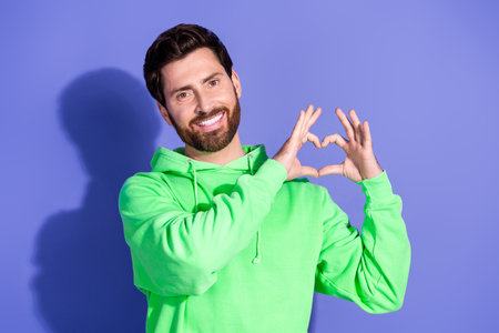 Photo portrait of handsome boyfriend smiling man wearing neon green hoodie showing heart symbol love...