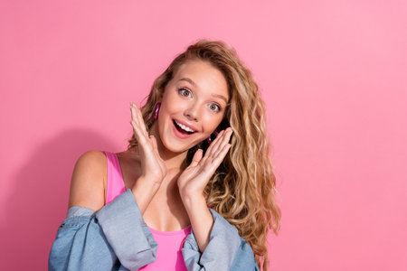 Joyful young woman in stylish denim and pink outfit exuding happiness and charm against vibrant pink backgroundの写真素材