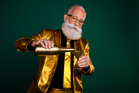 Elegant elderly man in golden glamour suit pouring drink at festive partyの写真素材